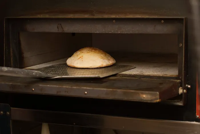Seesaminsiemenillä kuorrutettu leipä paistuu pizzauunissa lapion päällä.